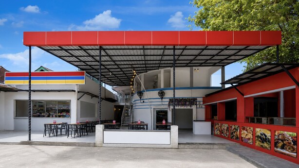 Un espacio de estar al aire libre techado con mesas y sillas, una escalera y vistas a un edificio con un letrero colorido.