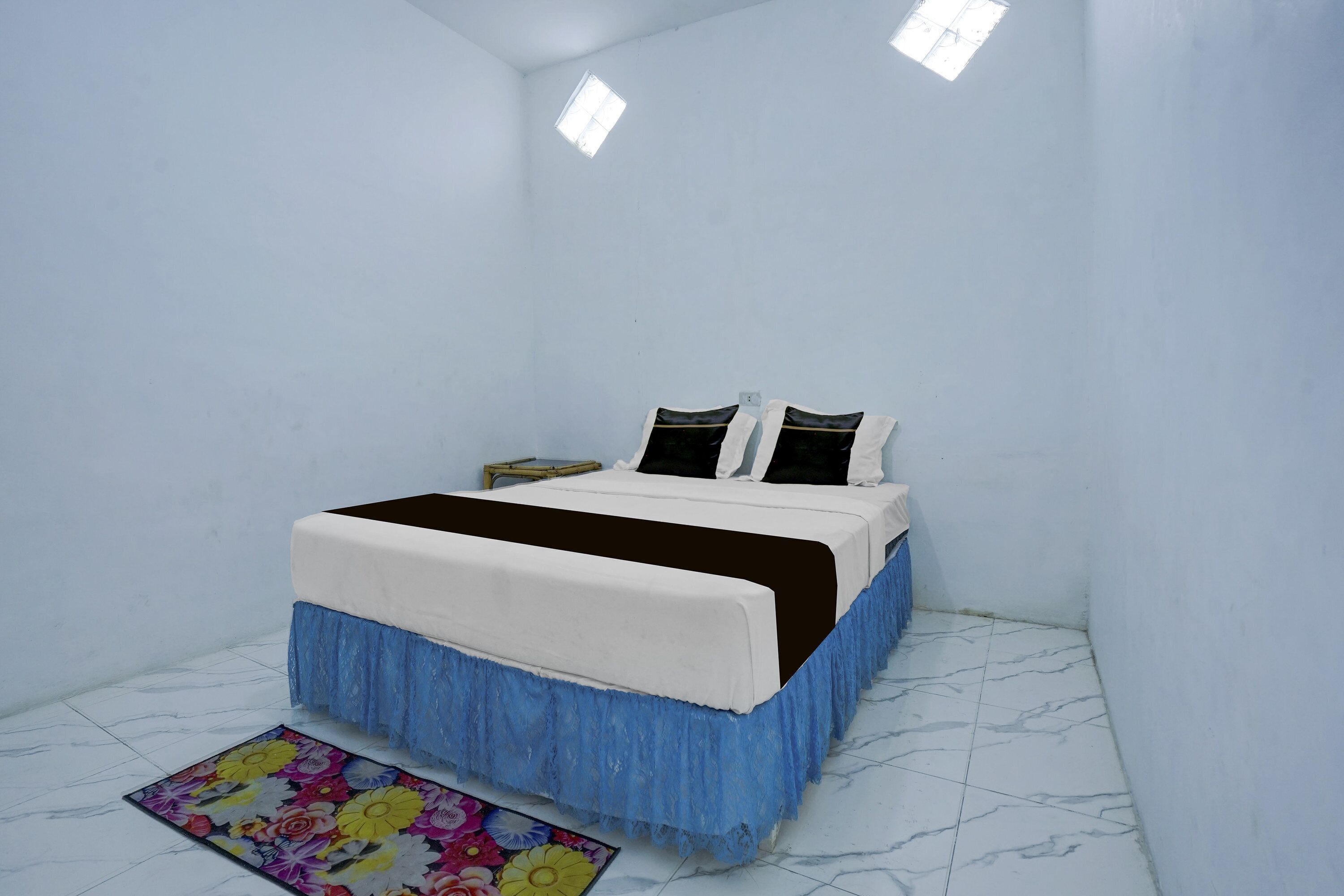 Un dormitorio con cama, mesita de noche, ventana y alfombra con estampado floral.