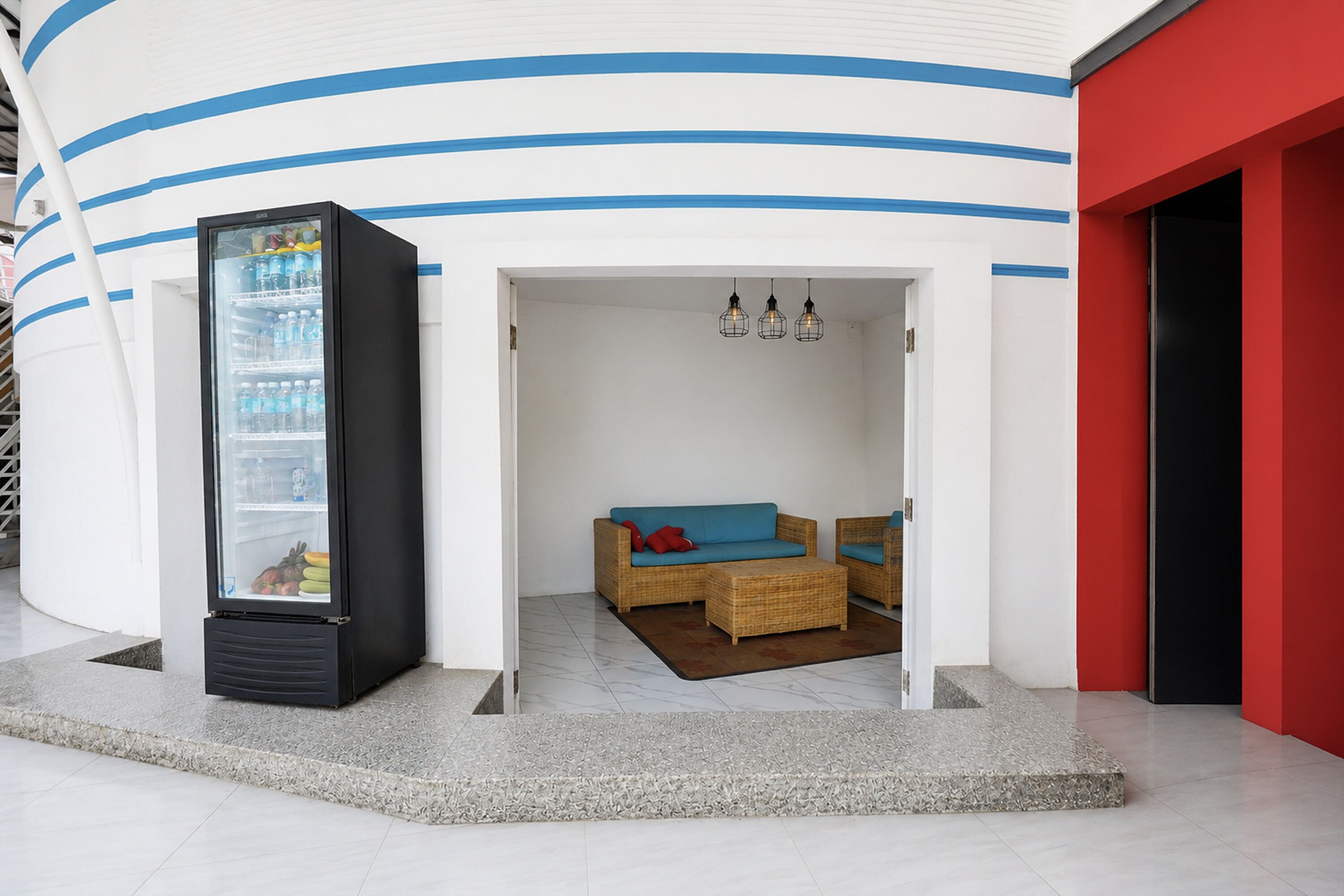 A modern interior with a seating area, a refrigerator, and a red wall.