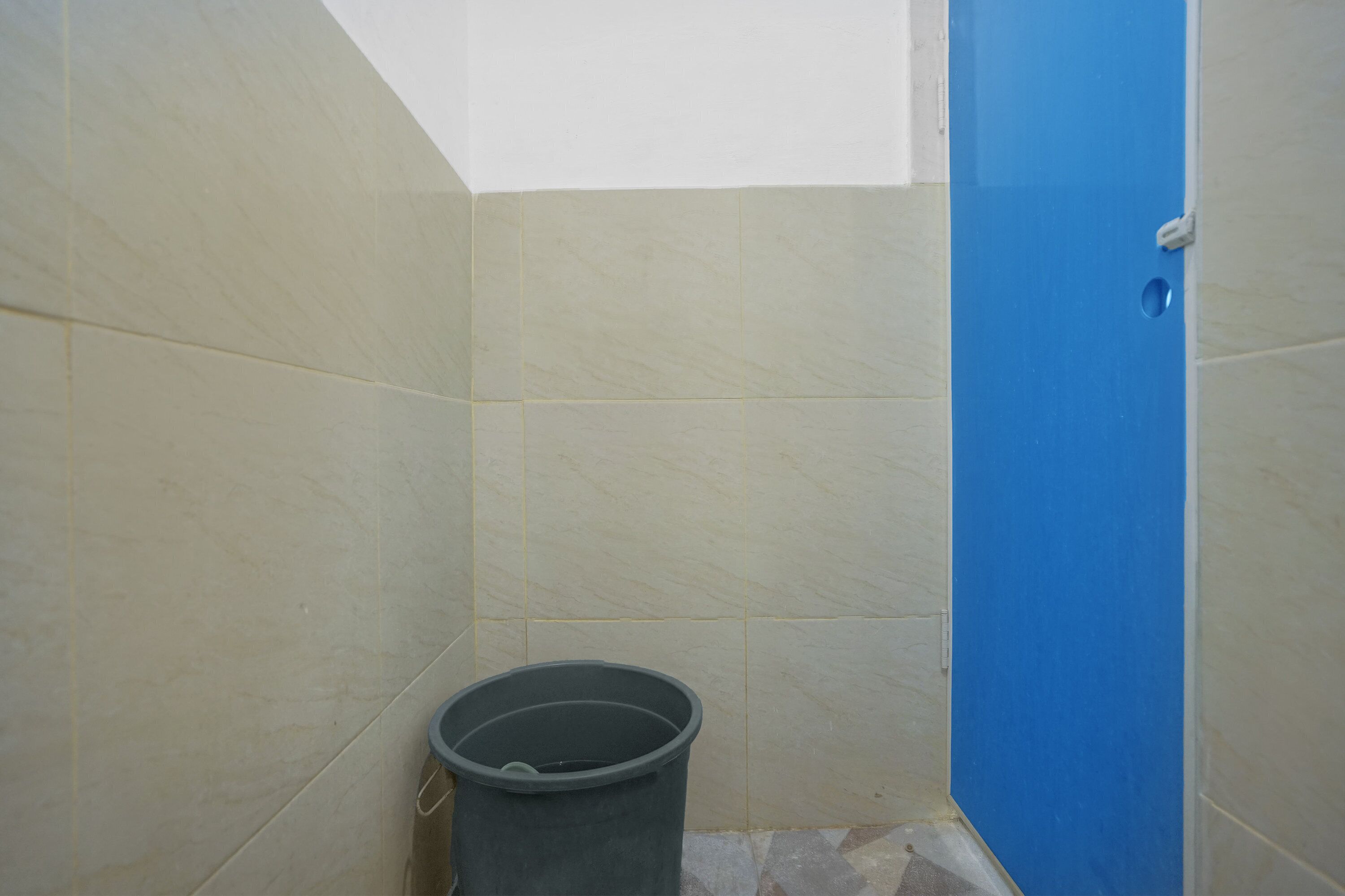 Un baño pequeño con azulejos color crema, una puerta azul y un cubo de basura negro.
