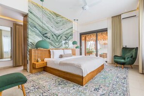 A modern bedroom with a large bed, a green armchair, a patterned rug, and a marble wall. - Siddhi Villa (Kerobokan)
