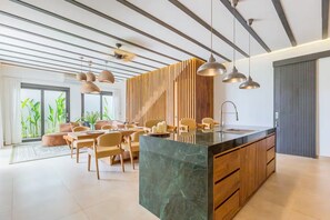 A modern kitchen with a marble island, pendant lighting, and a dining area with chairs and a sofa. - Siddhi Villa (Kerobokan)