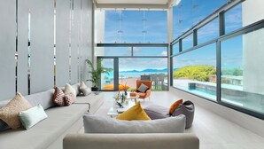 A modern living room with a large window, a sofa, a coffee table, and a view of a pool and mountains. - Luxury Sunset House Home Gym Cinema (Bophut)