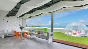 A modern outdoor seating area with a view of the ocean, a transparent dome structure, and a white wall with geometric patterns. - Luxury Sunset House Home Gym Cinema (Bophut)