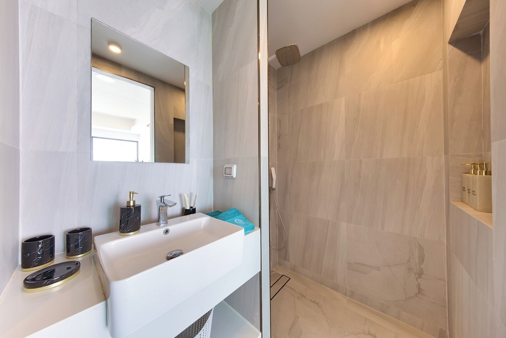 A bathroom with a white sink, a mirror, and a shower with beige tiles.