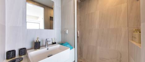 A bathroom with a white sink, a mirror, and a shower with beige tiles.