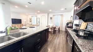 A modern kitchen with granite countertops, a built-in stove, and a dining area with a table and chairs. - Irvine Great Park Beacon 3 B &4 B two story house (Irvine)