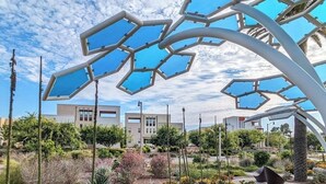 A landscaped garden with a geometric metal sculpture, a paved walkway, and modern buildings in the background. - Irvine Great Park Beacon 3 B &4 B two story house (Irvine)
