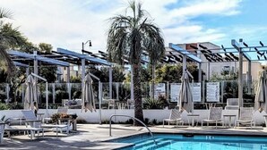 A swimming pool with lounge chairs and umbrellas, surrounded by palm trees and a clear sky. - Irvine Great Park Beacon 3 B &4 B two story house (Irvine)