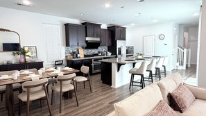 Una cocina moderna con armarios oscuros, una isla central y una zona de comedor con sillas y mesa.