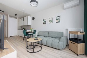 Ein modernes Wohnzimmer mit grauem Sofa, einem runden Holztisch, einem Fernseher und einer Küchenzeile.