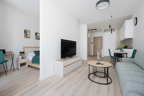 Ein modernes Wohnzimmer mit Flachbildfernseher, einer Couch, einem Essbereich mit Tisch und Stühlen sowie einer Küchenzeile mit Schränken und einer Arbeitsplatte.