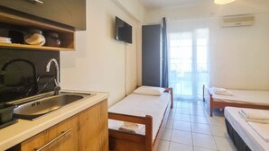 Habitación de hotel compacta con kitchenette, dos camas individuales, televisión y puerta corredera de vidrio al exterior.