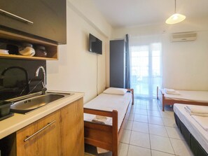 A compact hotel room with a kitchenette, two single beds, a TV, and a sliding glass door to the outside. - 104 - EVROSTAR Studio by SDR (Paralia)