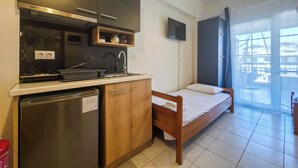 Cocina compacta equipada con refrigerador, microondas y pileta. Una cama está ubicada cerca de un ventanal amplio.