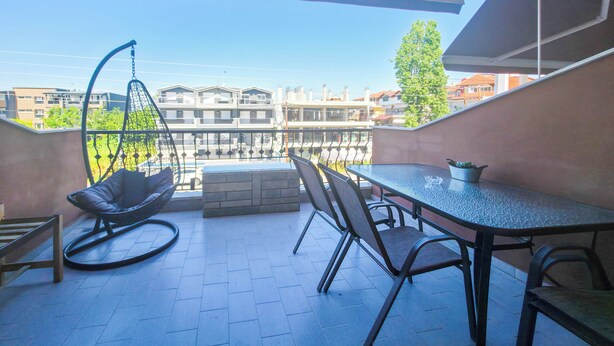 Un balcón con una silla colgante, una mesa y sillas, con vistas a un paisaje urbano.