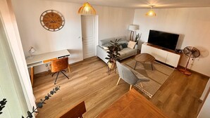 Een moderne woonkamer met een wit bureau, een grijze bank, een televisie en een plafondventilator.