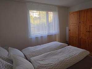 Ein Schlafzimmer mit zwei Betten, einem Fenster mit durchsichtigen Vorhängen und einem Holzschrank.
