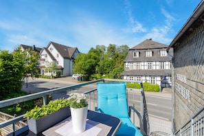 A balcony with a chair, a potted plant, and a view of a street with buildings. - Coerdt Apartment in Olsberg with Beautiful Balcony (Olsberg)