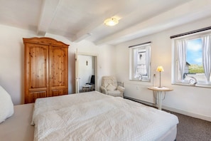 A bedroom with a large bed, a wooden wardrobe, a chair, a small table with a lamp, and a window with curtains. - Coerdt Apartment in Olsberg with Beautiful Balcony (Olsberg)