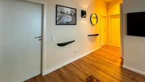 Un pasillo con una puerta blanca, una fotografía enmarco, un espejo redondo y un televisor negro en la pared.