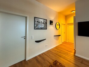 Ein Korridor mit einer weißen Tür, einem gerahmten Foto, einem runden Spiegel und einem schwarzen Fernseher an der Wand.