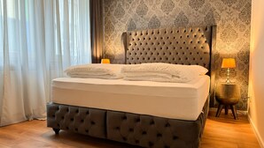 Una cama con cabecera capitonada, lámpara de noche y papel tapiz estampado.