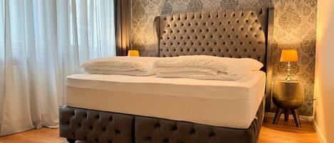 A bed with a tufted headboard, a bedside lamp, and a patterned wallpaper.