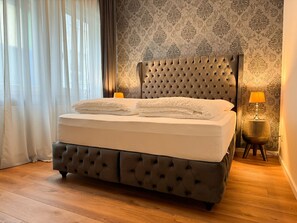Ein Bett mit einer gepolsterten Kopfteile, einer Nachttischlampe und einer Wand mit Muster.
