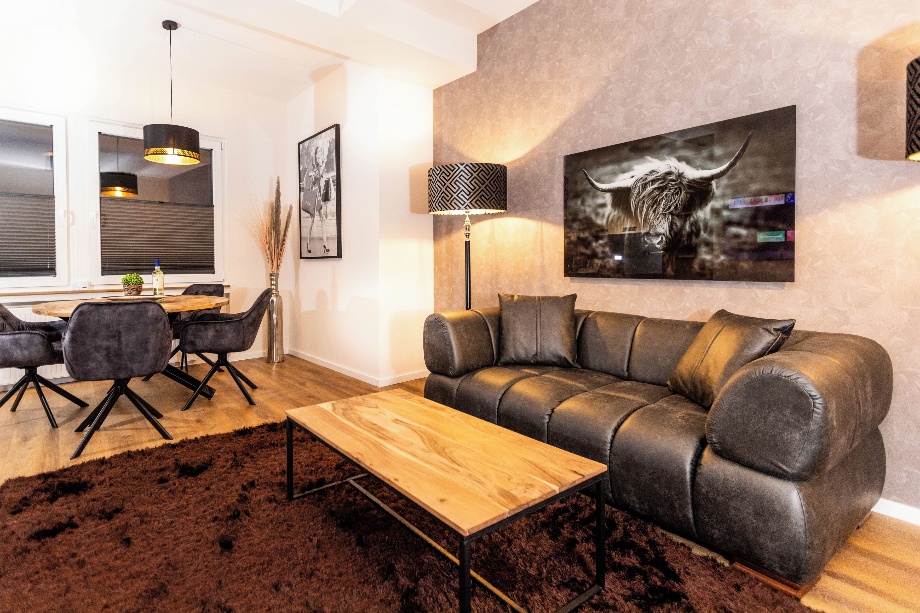 Un salon moderne avec un canapé en cuir, une table basse en bois et un coin repas comprenant une table et des chaises.
