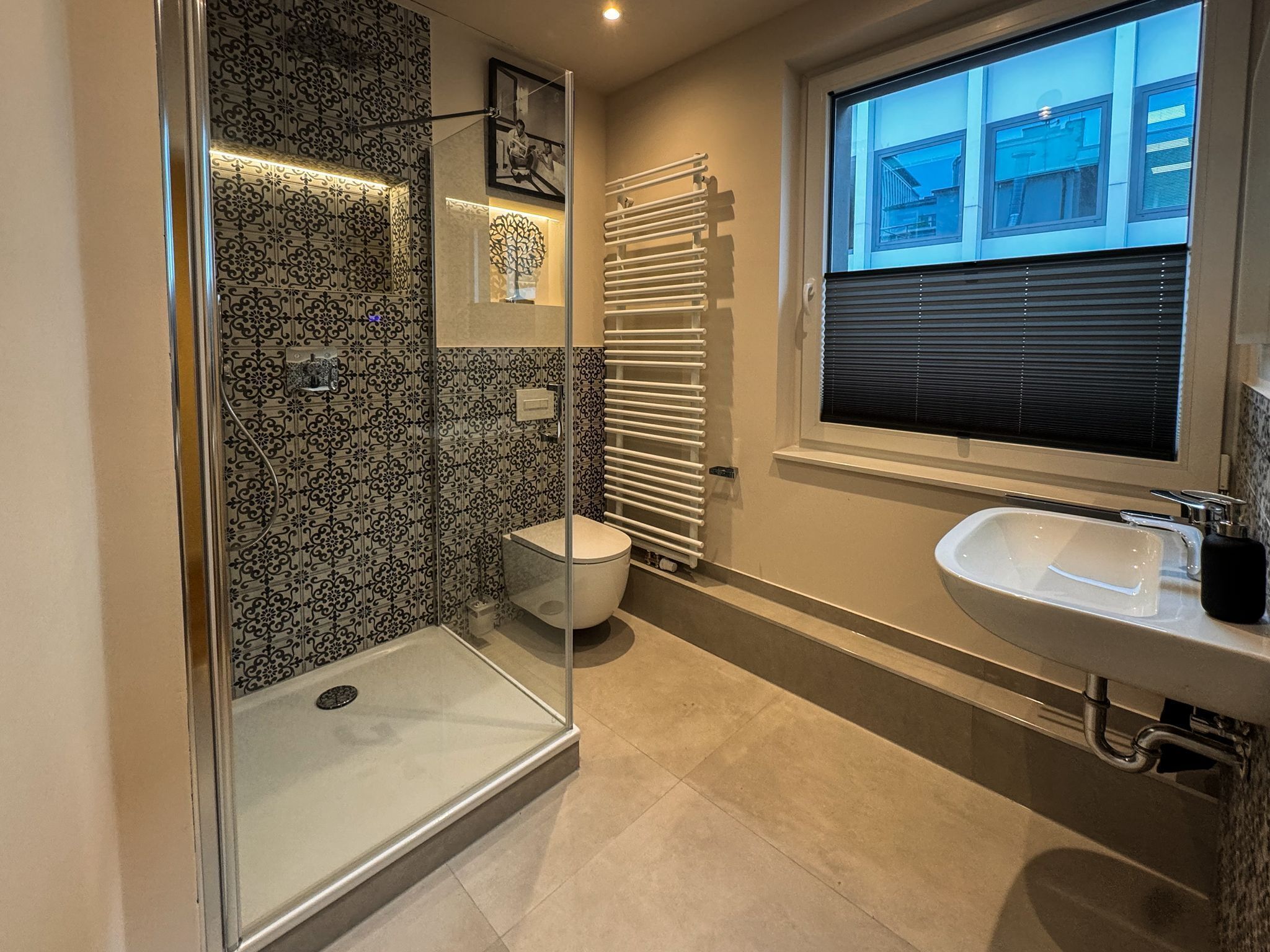 Ein modernes Badezimmer mit Duschkabine aus Glas, Toilette, Handtuchheizkörper und Waschbecken.