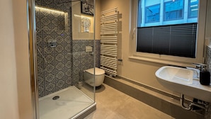Un baño moderno con cabina de ducha de vidrio, inodoro, radiador y lavamanos.
