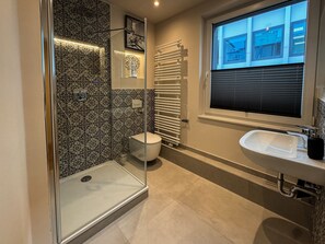 Ein modernes Badezimmer mit Duschkabine aus Glas, Toilette, Handtuchheizkörper und Waschbecken.