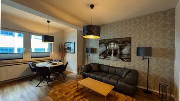 Ein modernes Wohnzimmer mit Sofa, Couchtisch, Essbereich mit Tisch und Stühlen sowie einem großen Gemälde an der Wand.