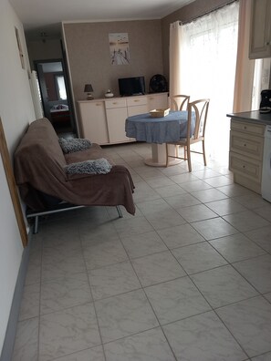 Ein Zimmer mit Bett, Tisch, Stuhl, Fernseher und einer Küchenzeile.