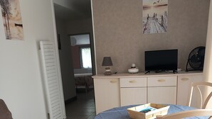 Ein Zimmer mit einem Bett, einem Tisch mit blauer Tischdecke, einem Fernseher, einer Lampe und einem Ventilator.