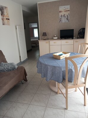 Ein Zimmer mit einem Bett, einem Tisch mit blauer Tischdecke, einem Fernseher, einer Lampe und einem Ventilator.
