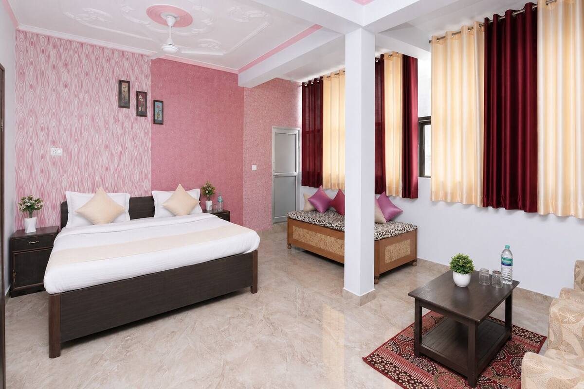 A hotel room with a bed, bedside tables, a sofa, a small table, and curtains.