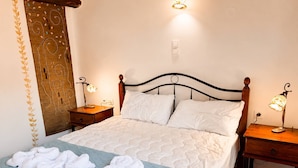 Uma cama bem arrumada com lençóis brancos e colcha azul, duas mesas de cabeceira com abajures, um cabeceira de madeira e um painel decorativo na parede.