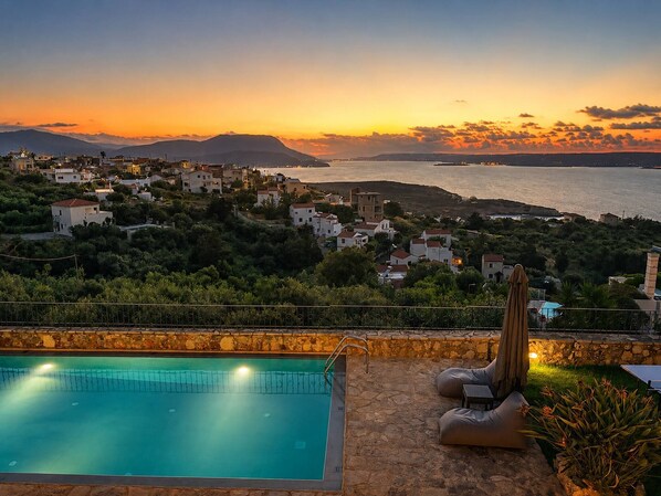 Ein Pool mit einer Steindeck, einem Kaktus und Blick auf eine Küstenstadt im Sonnenuntergang.