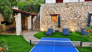 Mesa de pingue-pongue em um jardim com paredes de pedra e área de estar ao ar livre.