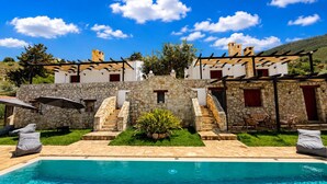 Área da piscina com uma escadaria de pedra que leva a um edifício, mobiliário de exterior e um céu azul límpido.