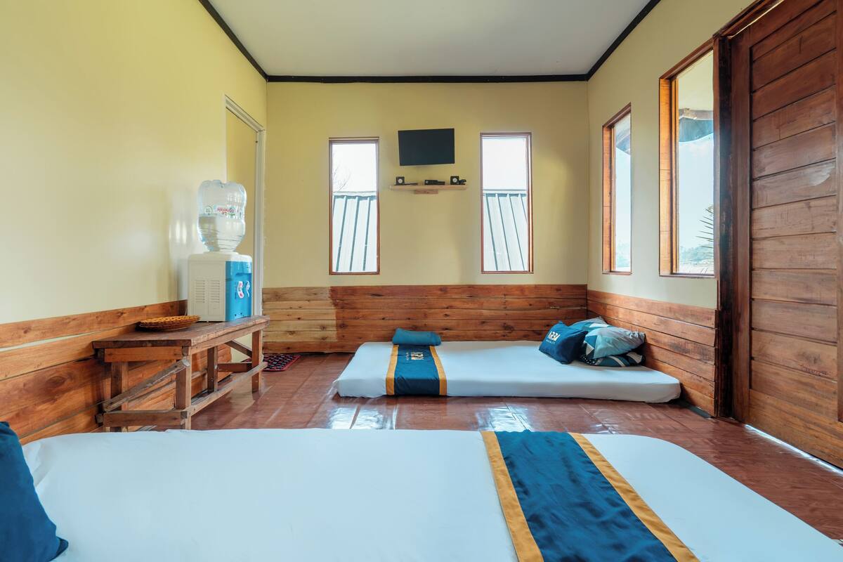A room with two beds, a wooden bench, a water dispenser, and a TV mounted on the wall.