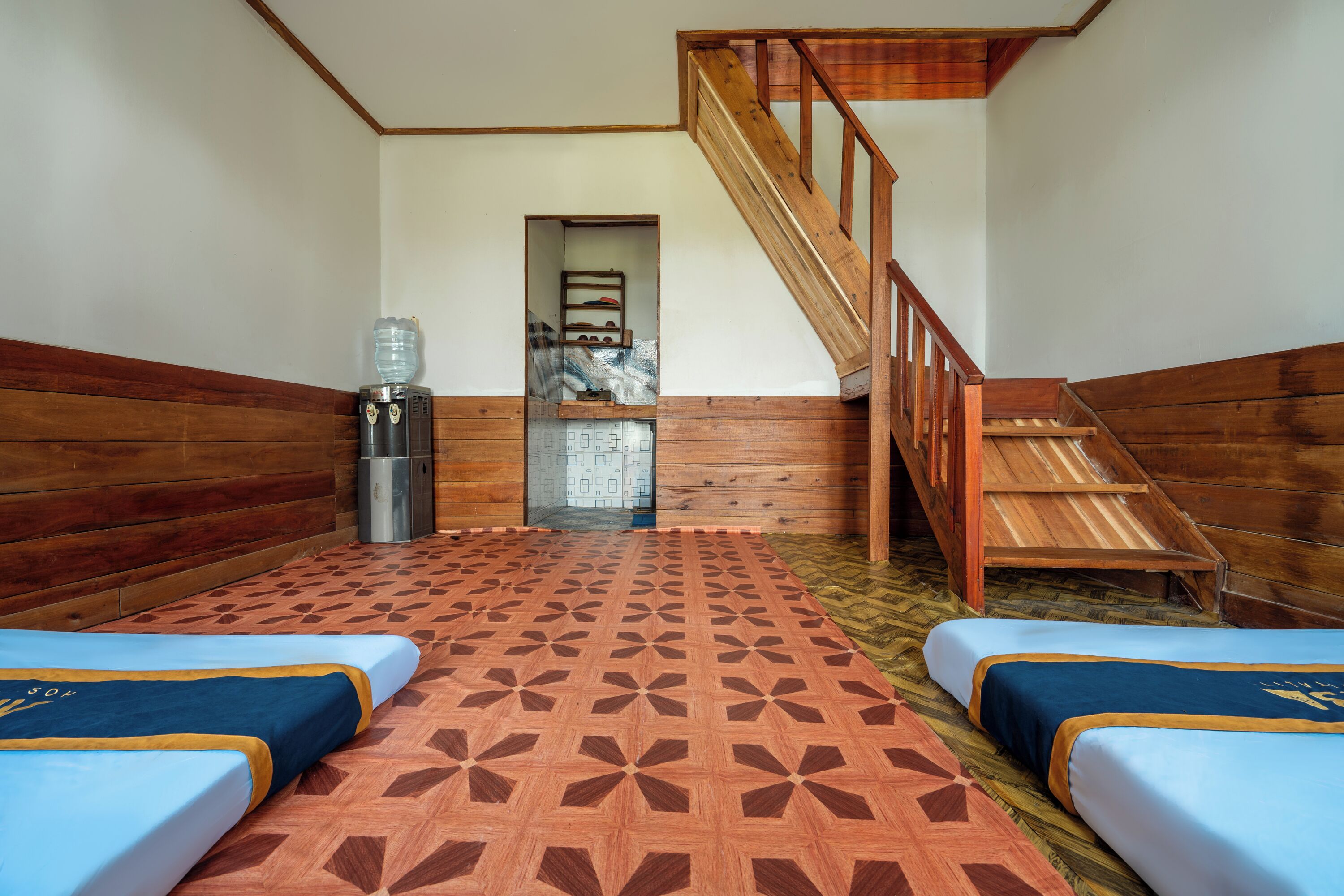 A room with two beds, a wooden staircase, and a small kitchenette.