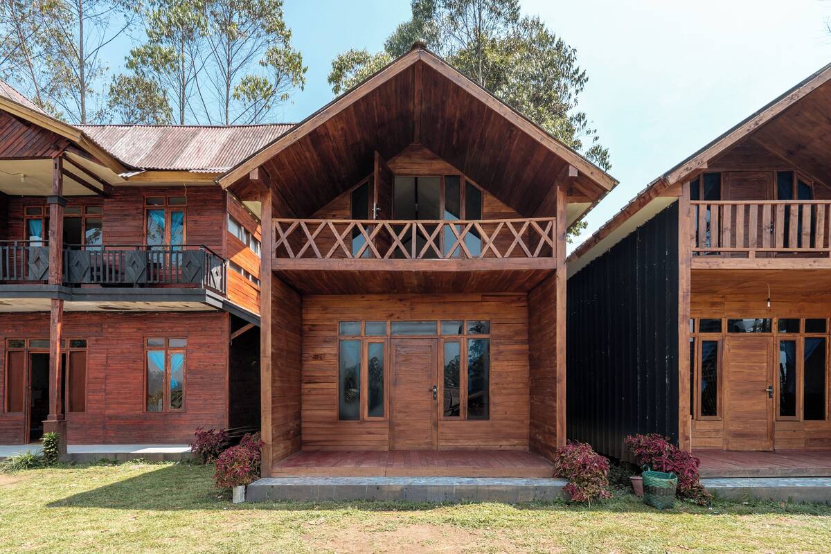 A wooden cabin with a balcony, large windows, and a porch area.