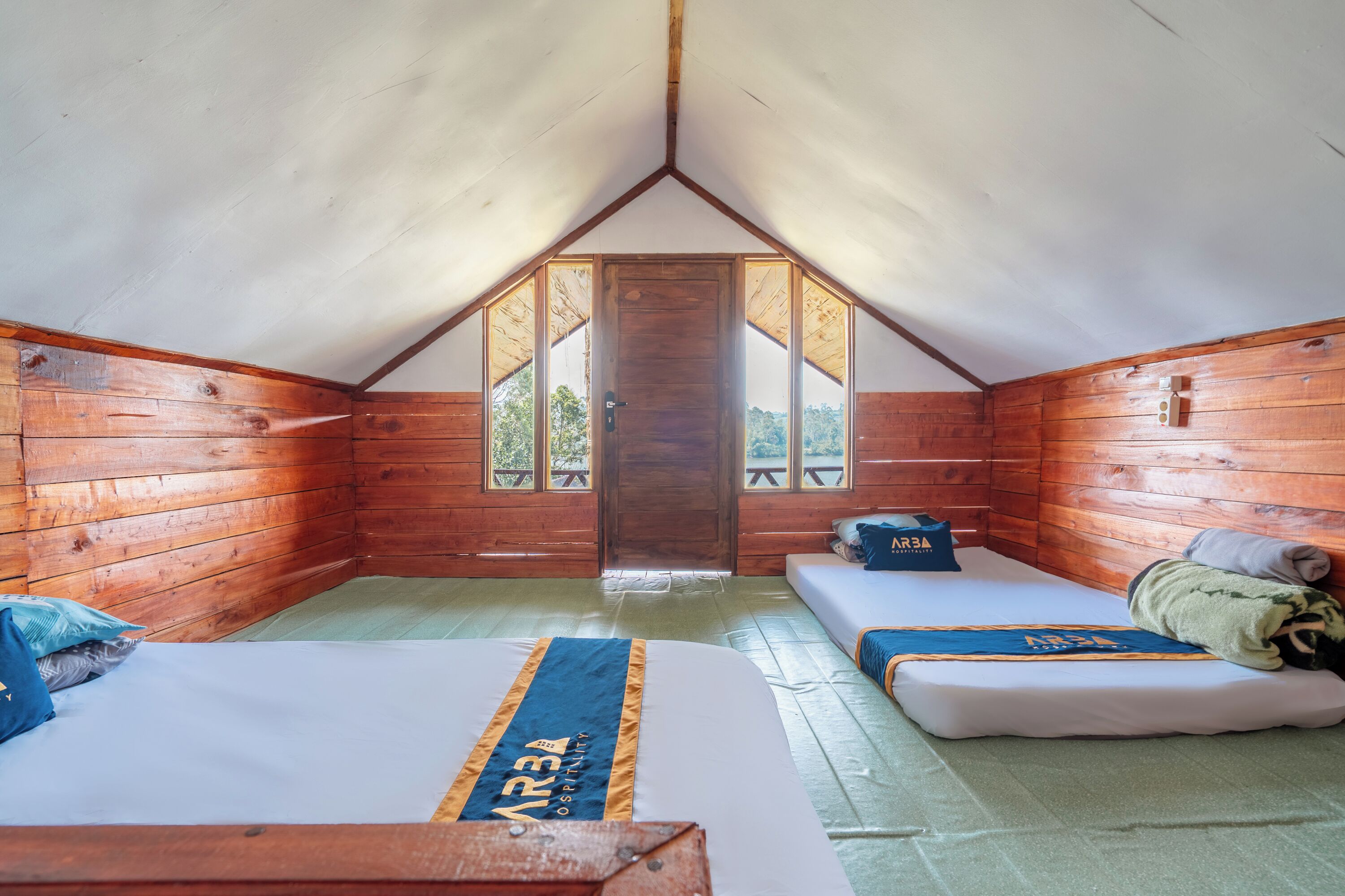 Une petite pièce en bois, aménagée comme une cabane, avec un plafond en pente, deux lits, un banc et une porte donnant sur l’extérieur.