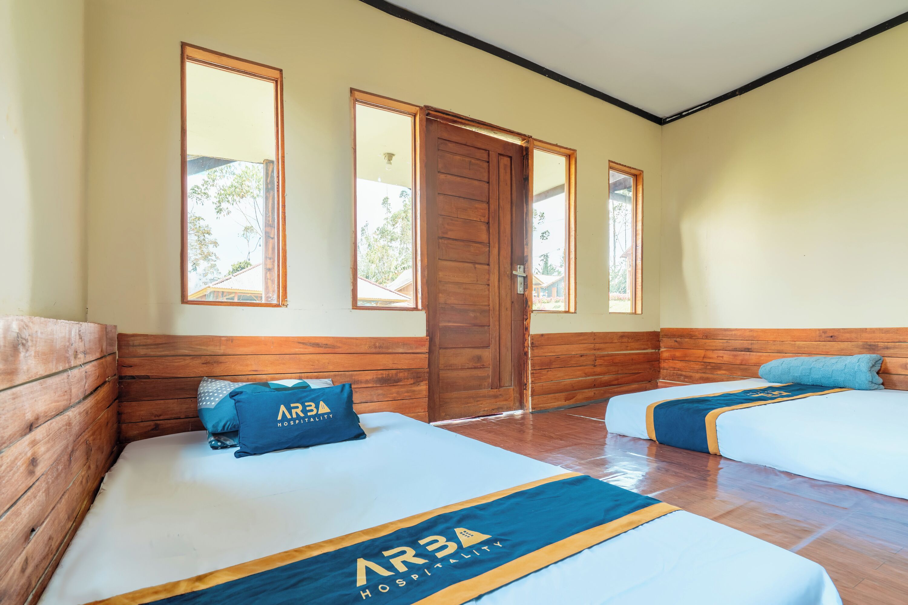 A hotel room with two beds, wooden headboards, a large wooden door, and windows.