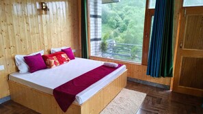 A wooden-paneled room with a large bed, a window with curtains, and a view of greenery outside. - Devine Hill (Shangarh)