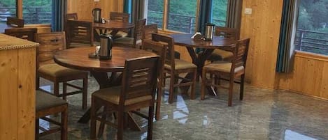 Un comedor con mesas y sillas de madera, ventanas amplias y una araña.