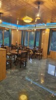 Uma sala de jantar com mesas e cadeiras de madeira, grandes janelas e um lustre.